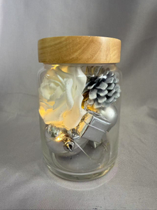 保留的花束在密封的玻璃罐中，带有银闪烁的线灯（AA×2电池供电），上面装饰着白玫瑰，银浆果，球体，礼品盒，松果和干草