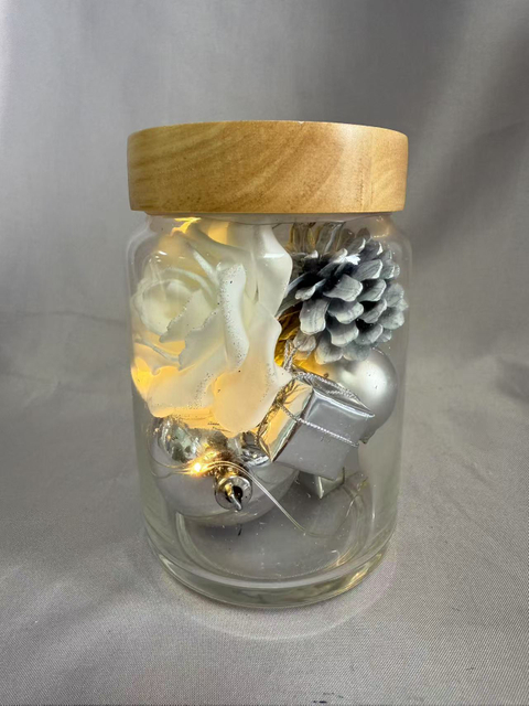 保留的花束在密封的玻璃罐中，带有银闪烁的线灯（AA×2电池供电），上面装饰着白玫瑰，银浆果，球体，礼品盒，松果和干草